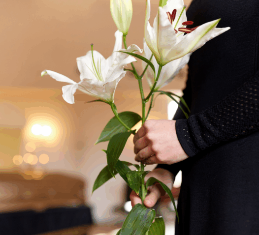 Person i svart klänning håller vita liljor i en kyrka.
