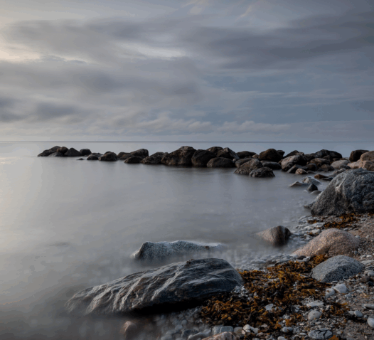 Klippor vid kusten under en mulen himmel, med havet i bakgrunden.